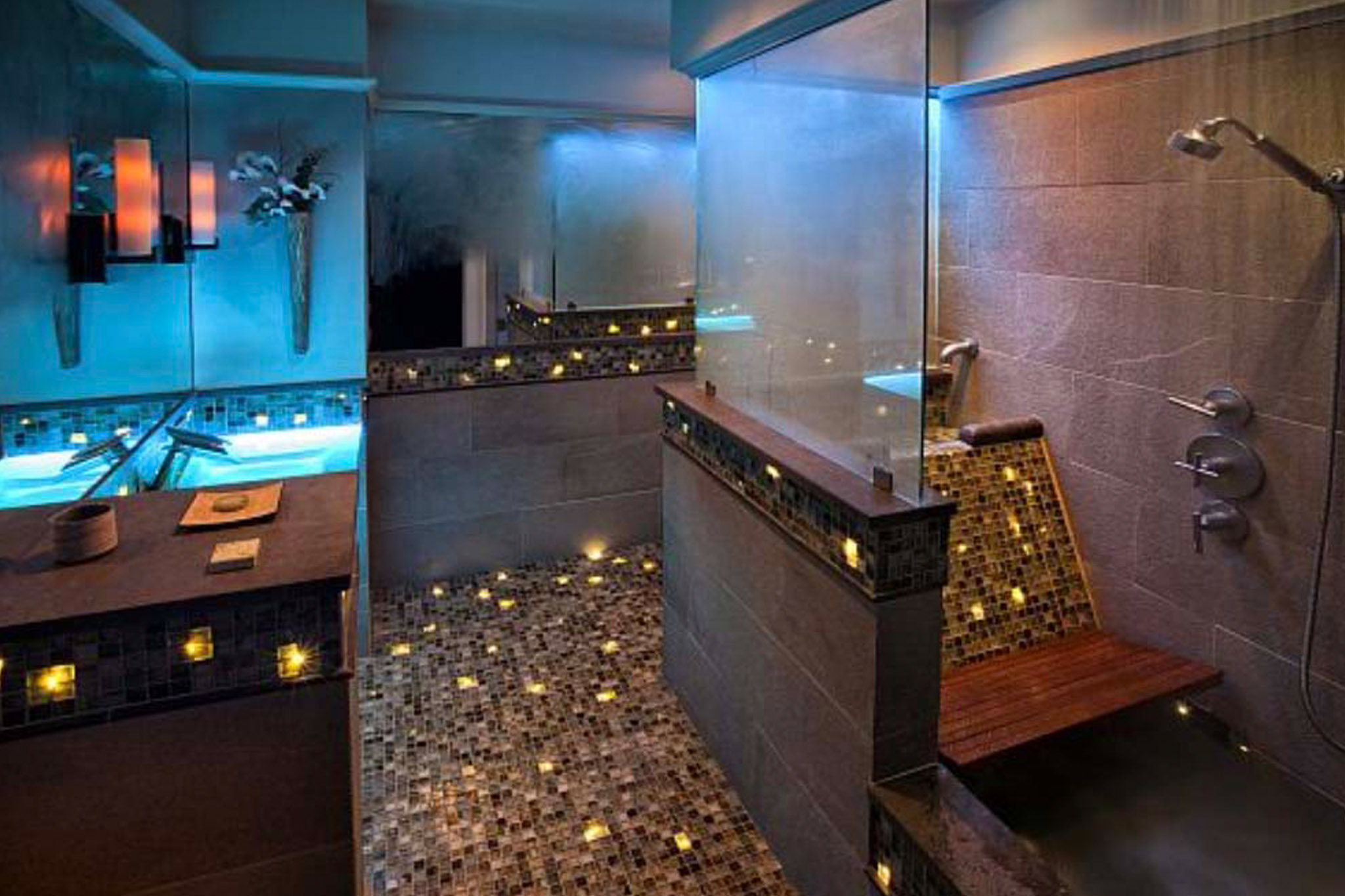 A luxurious bath with colorful fiber optic lighting, blue-lit glass sink, a roman bath and a rain head shower.