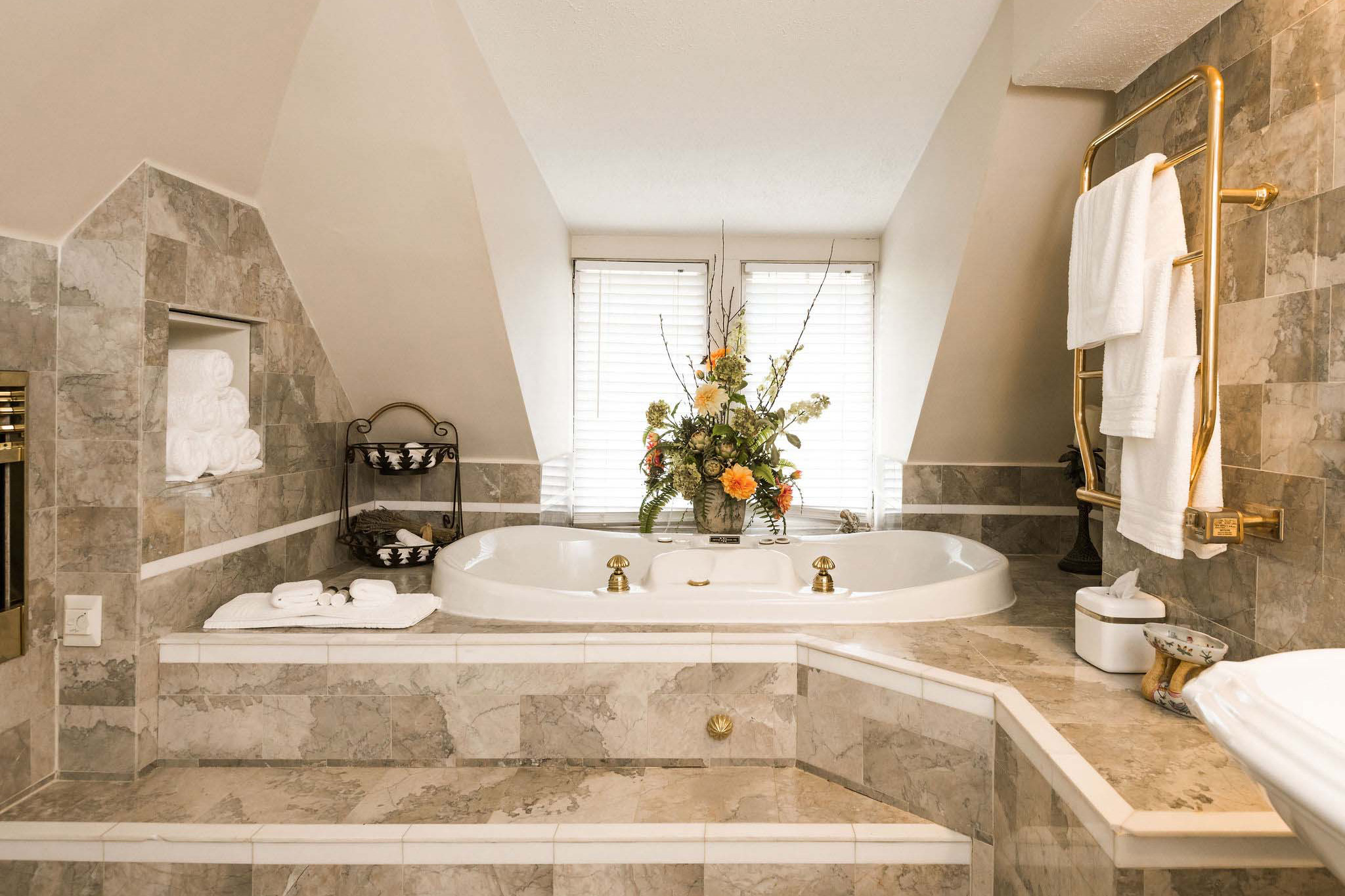 A luxurious white marble bathroom with heated floors and an elevated two-person Whirlpool bathtub, part of a 5-room suite in an Asheville bnb.