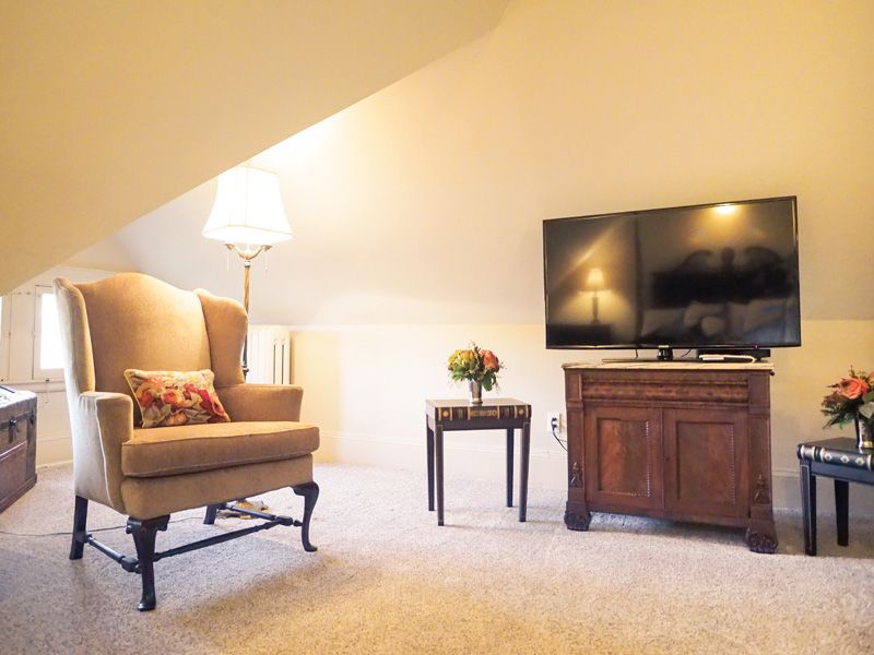 A relaxing corner in the attic with a TV, armchair, standing lamp and two small side tables.