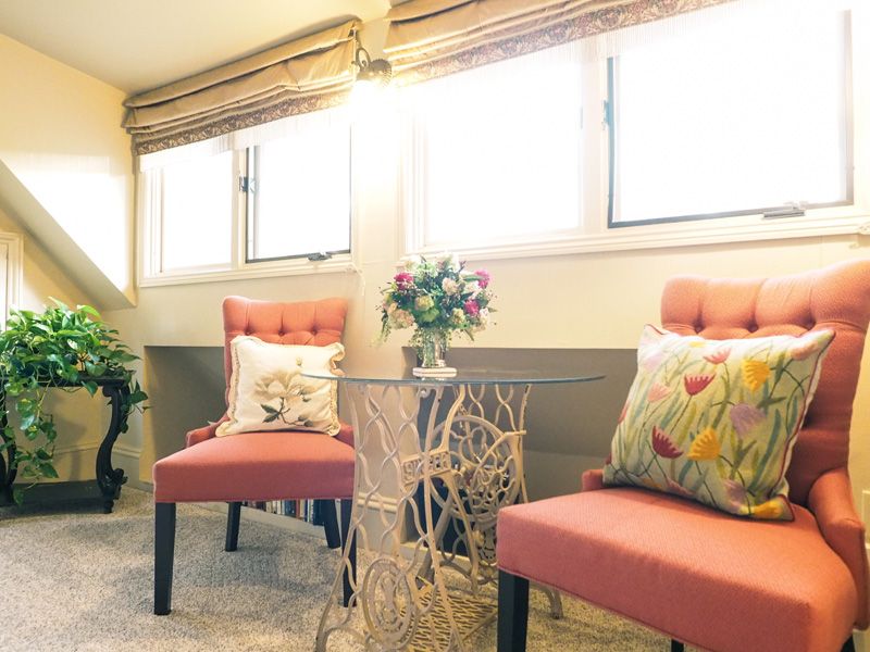 A relaxing area at one of the suites in the Asheville bed and breakfast. Two armchairs with floral pillows with a table and a flower bouquet.