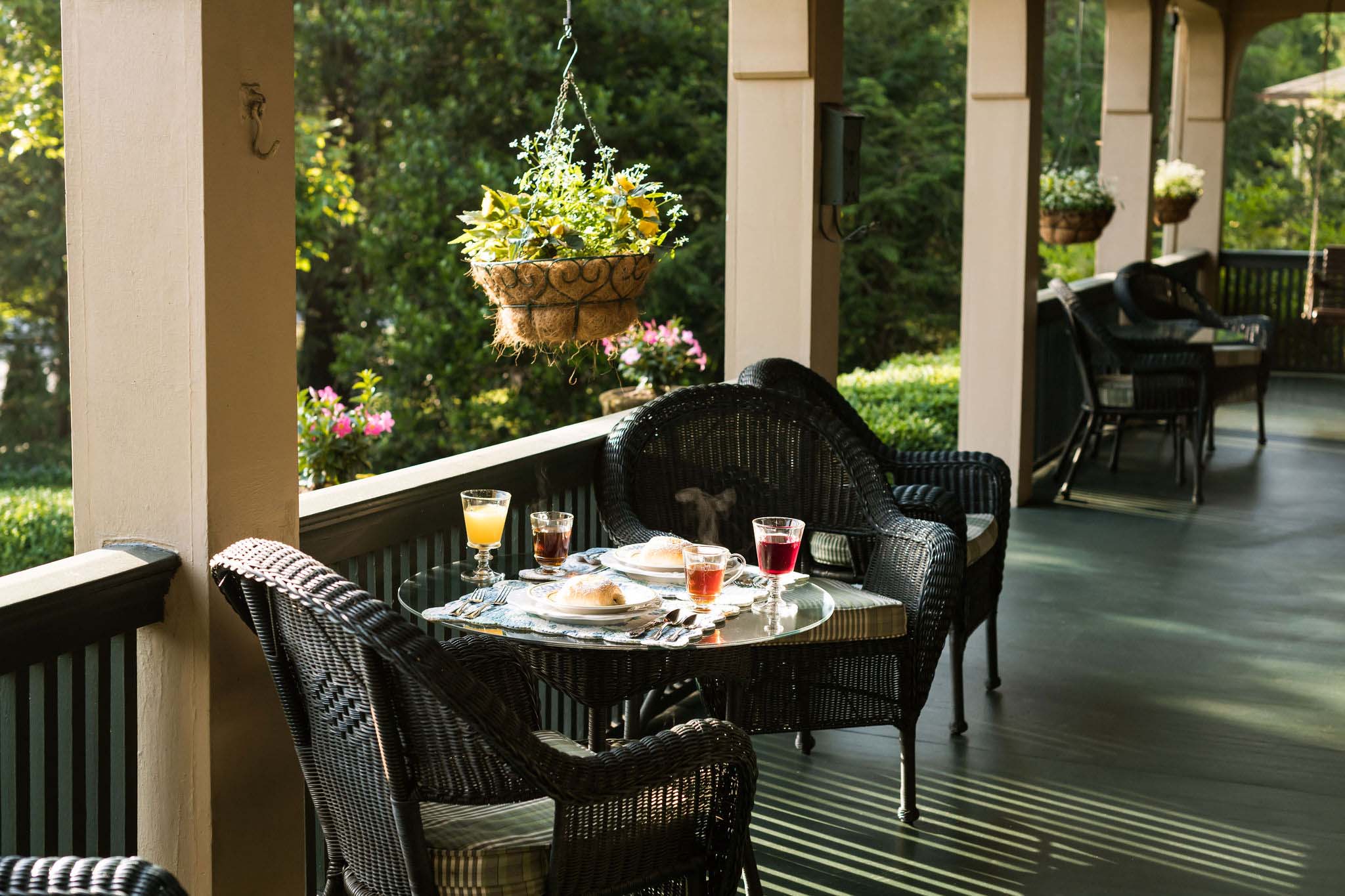 Outdoor breakfast on the bnb's porch. Rattan chairs with a table set for two. A yellow pot hanging from one of the Inn's arches.