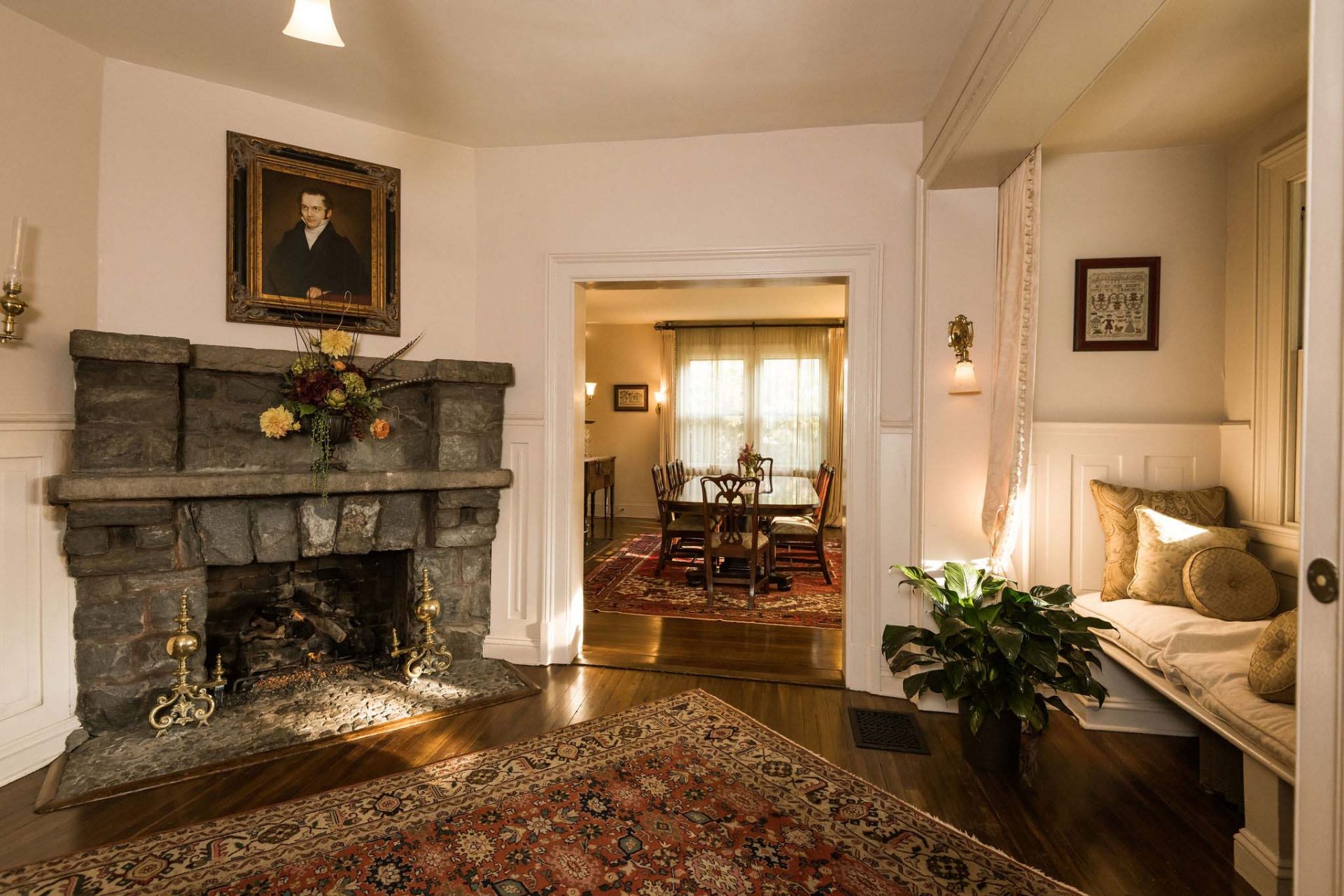 The Inn's foyer with a nook to the right, followed by the entrance to the dining area, and with a big stone fireplace and a portrait hanging above it.