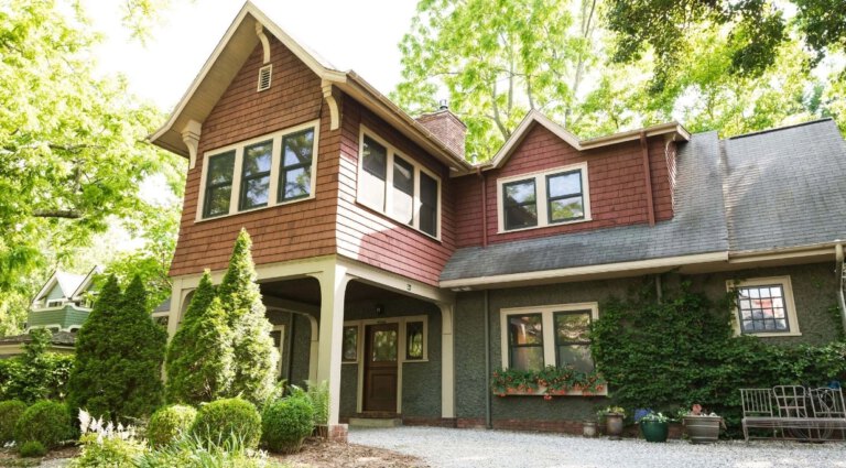 The front side of the carriage house behind the main house. Surrounded by green tree, with a backyard garden in the middle of a gravel square.