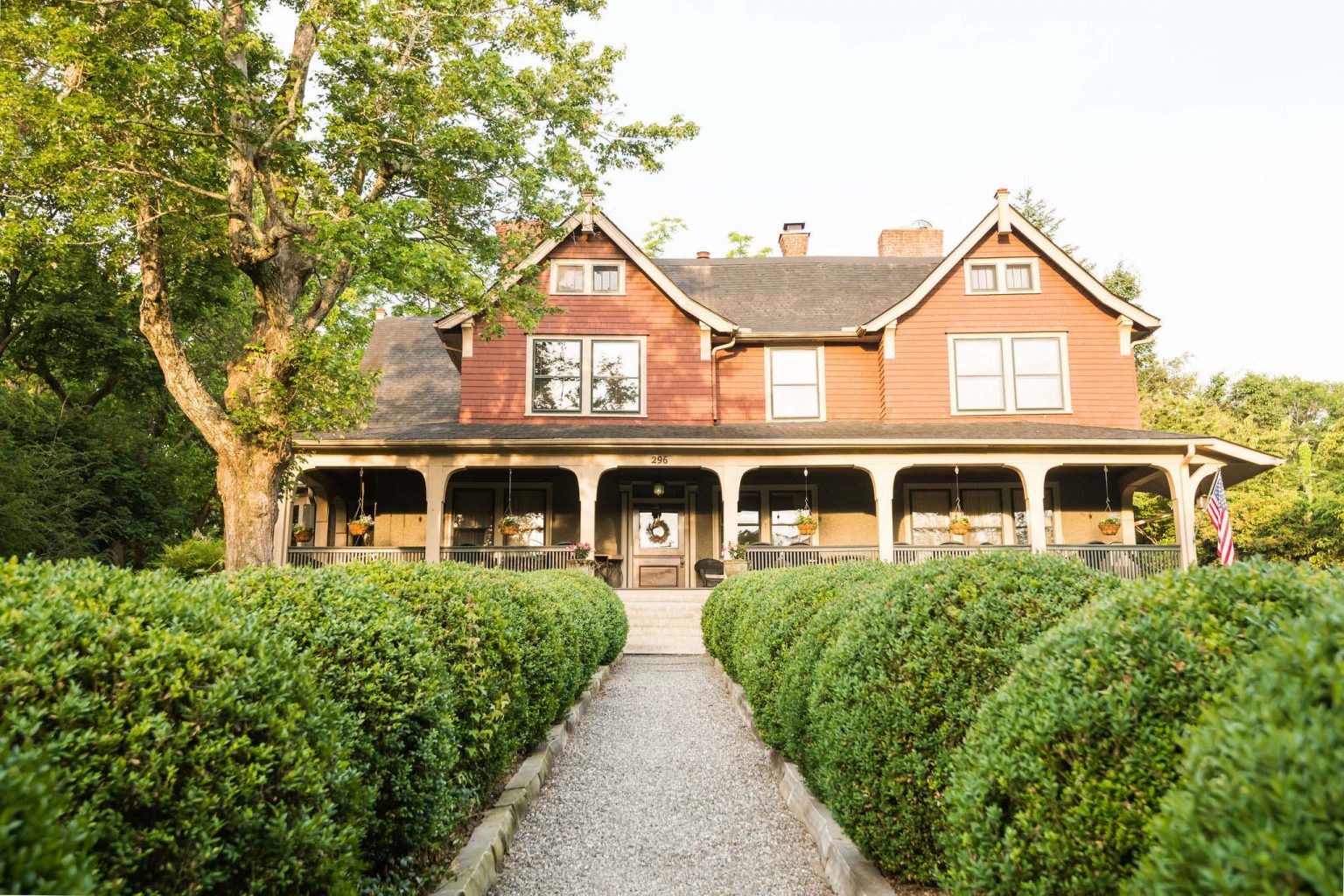 The front facade of the Asheville bed and breakfast with a gravel road with two rows of round ball bushed leading to the main entrance.