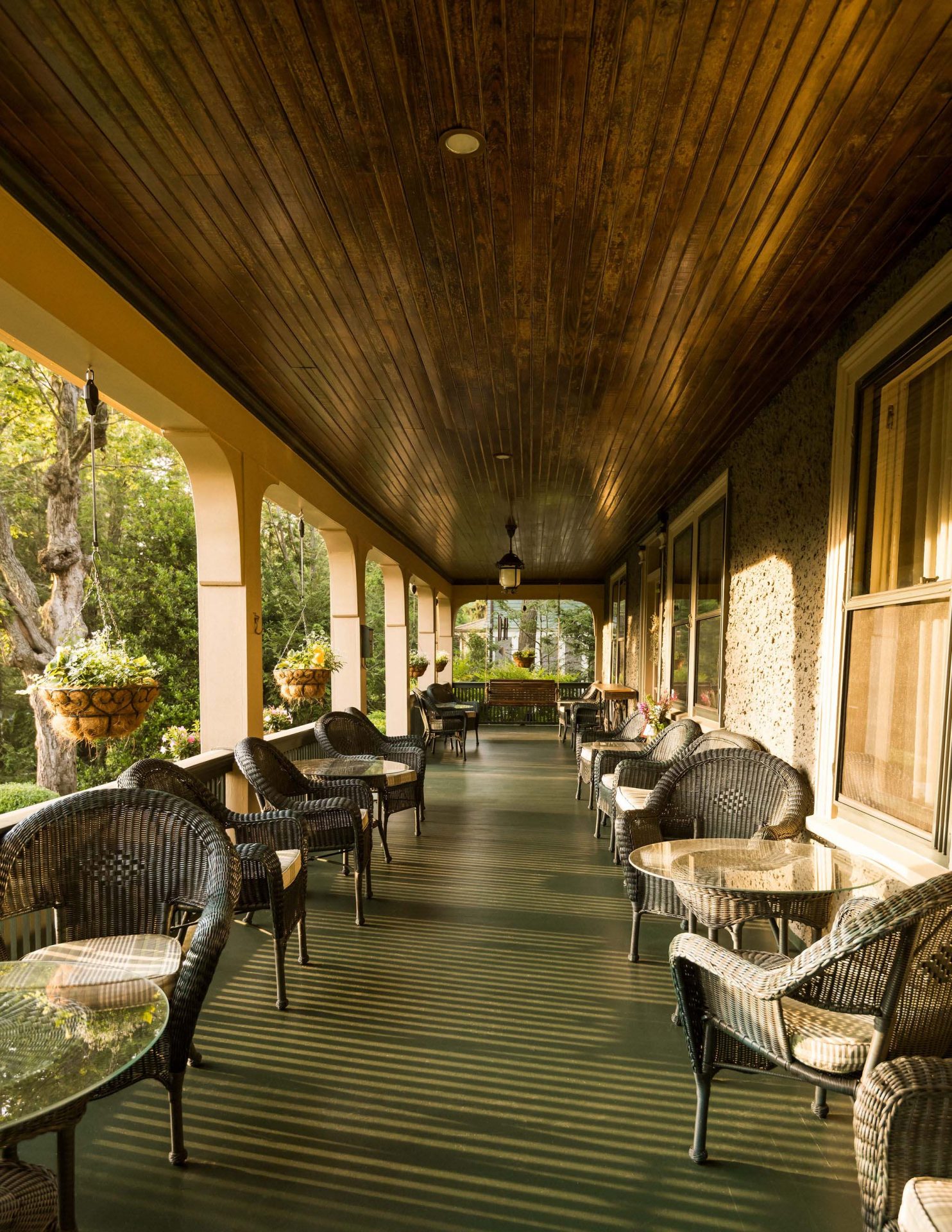 The front porch of the Inn with a wooden brown ceiling and two rows of rattan chairs and tables.