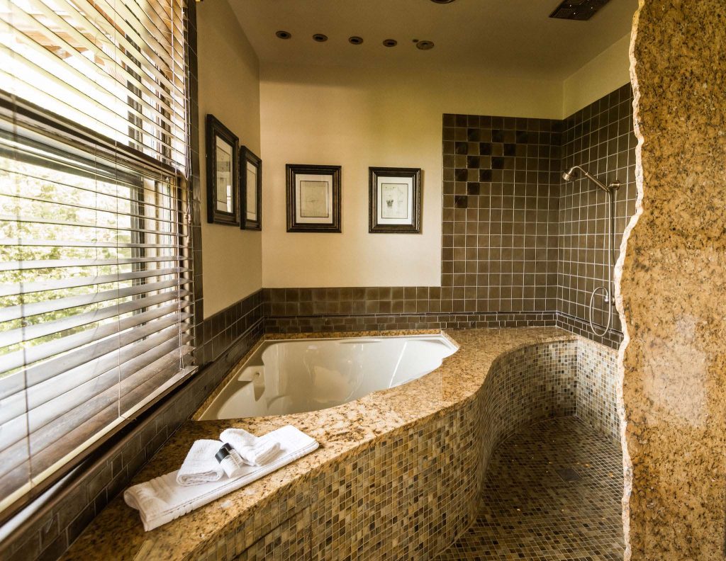 A two-Person jetted airbath tub with chromatherapy lights, marble countertops, and tiled floors. A romantic bath for a romantic Asheville getaway, captured in a daylight.