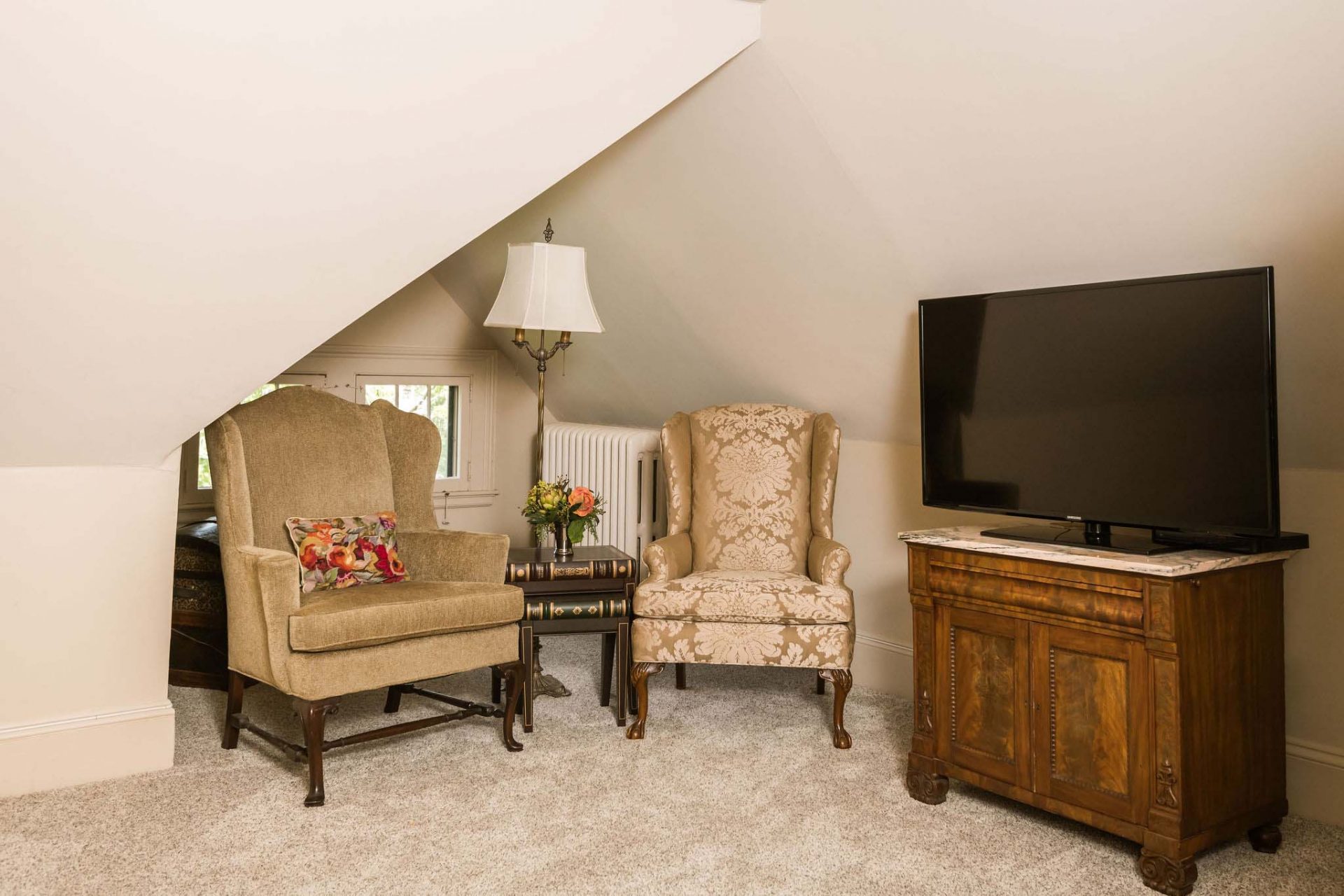 A carpeted relaxing area in the attic with two armchairs, a standing lamp and TV.