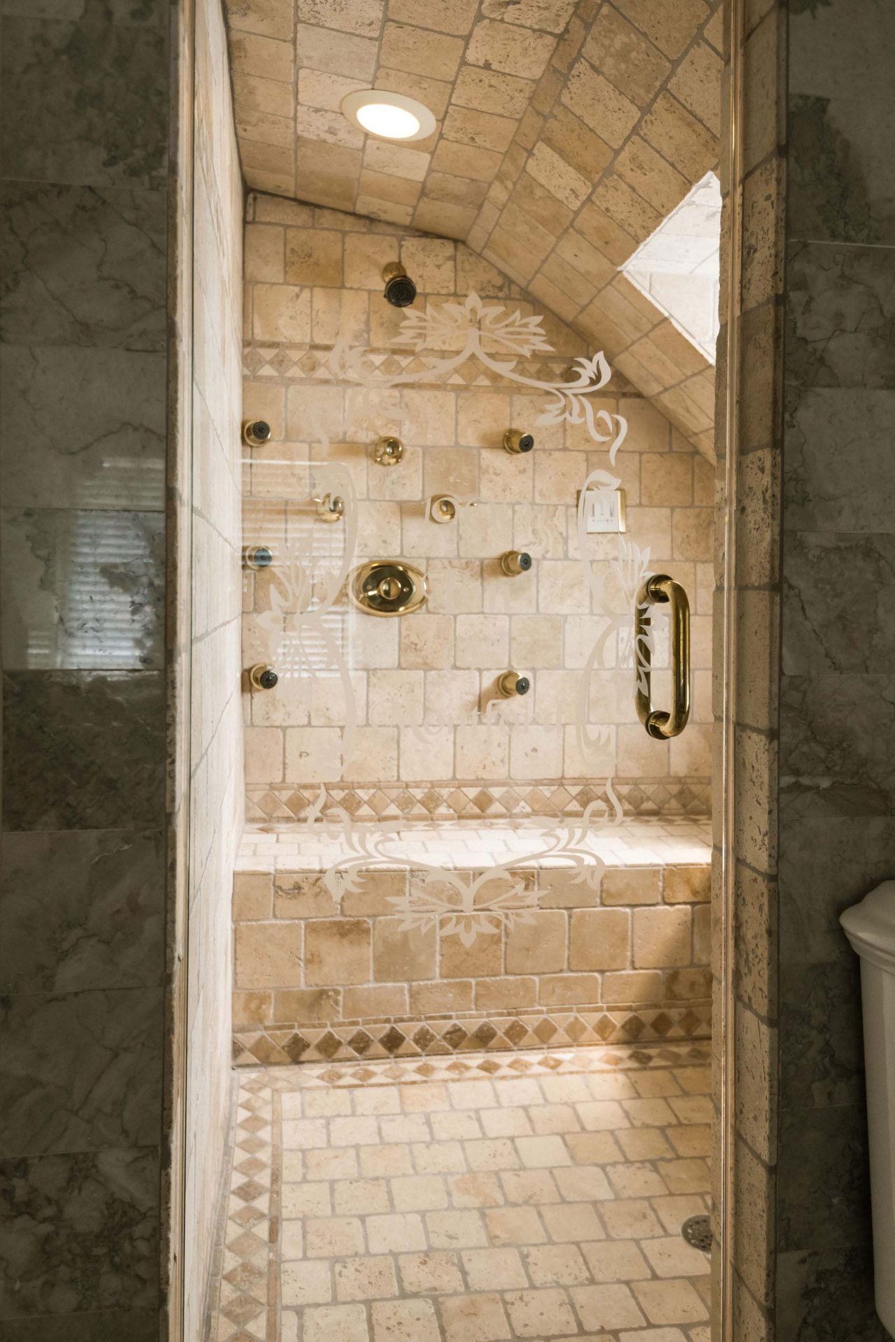 Private bathroom with beige, decorative tiles and a glass door, with a steam shower with multiple body jets.