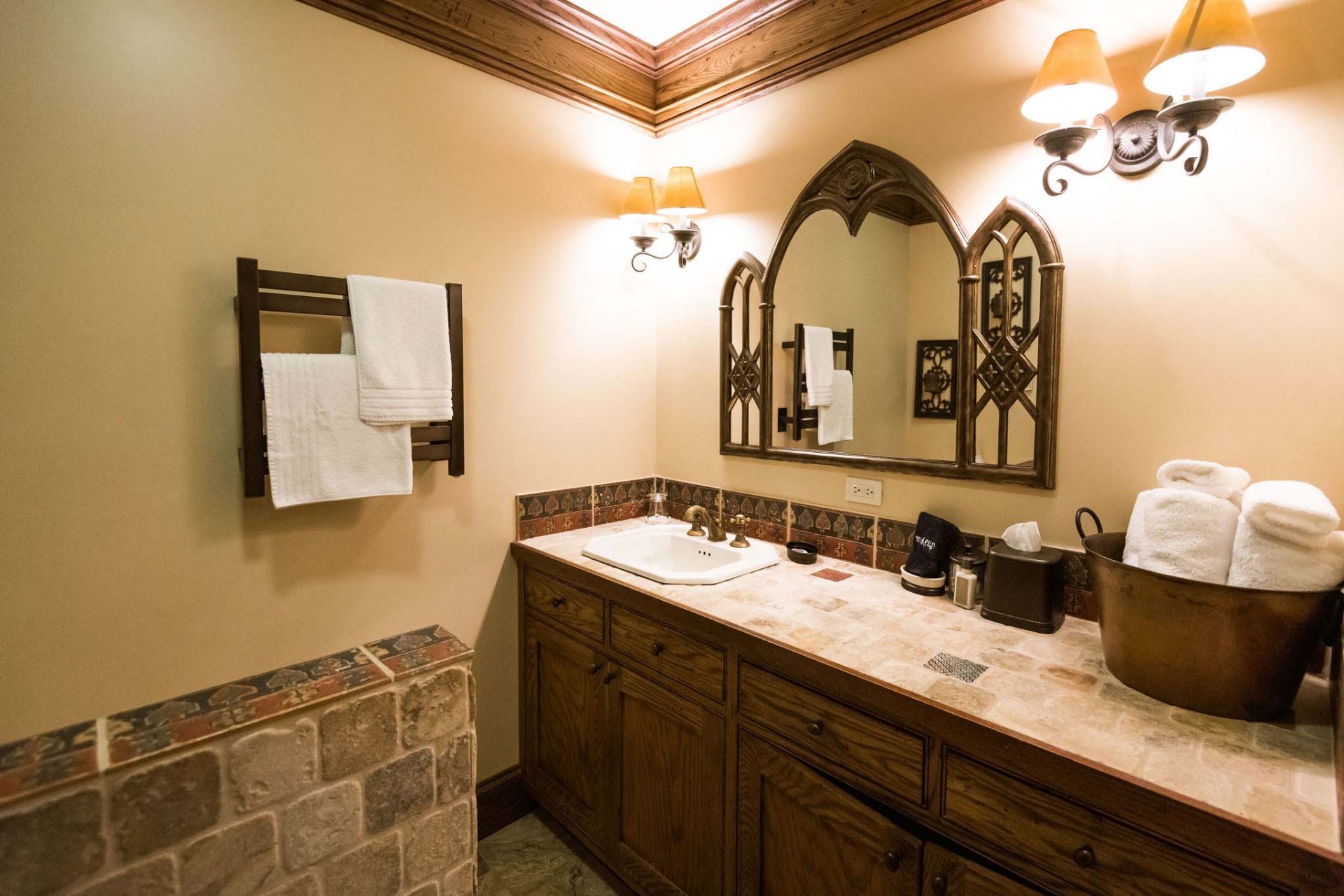 A bathroom with a long set of wooden dressers, stone countertop, and a decorative, gothic style mirror.
