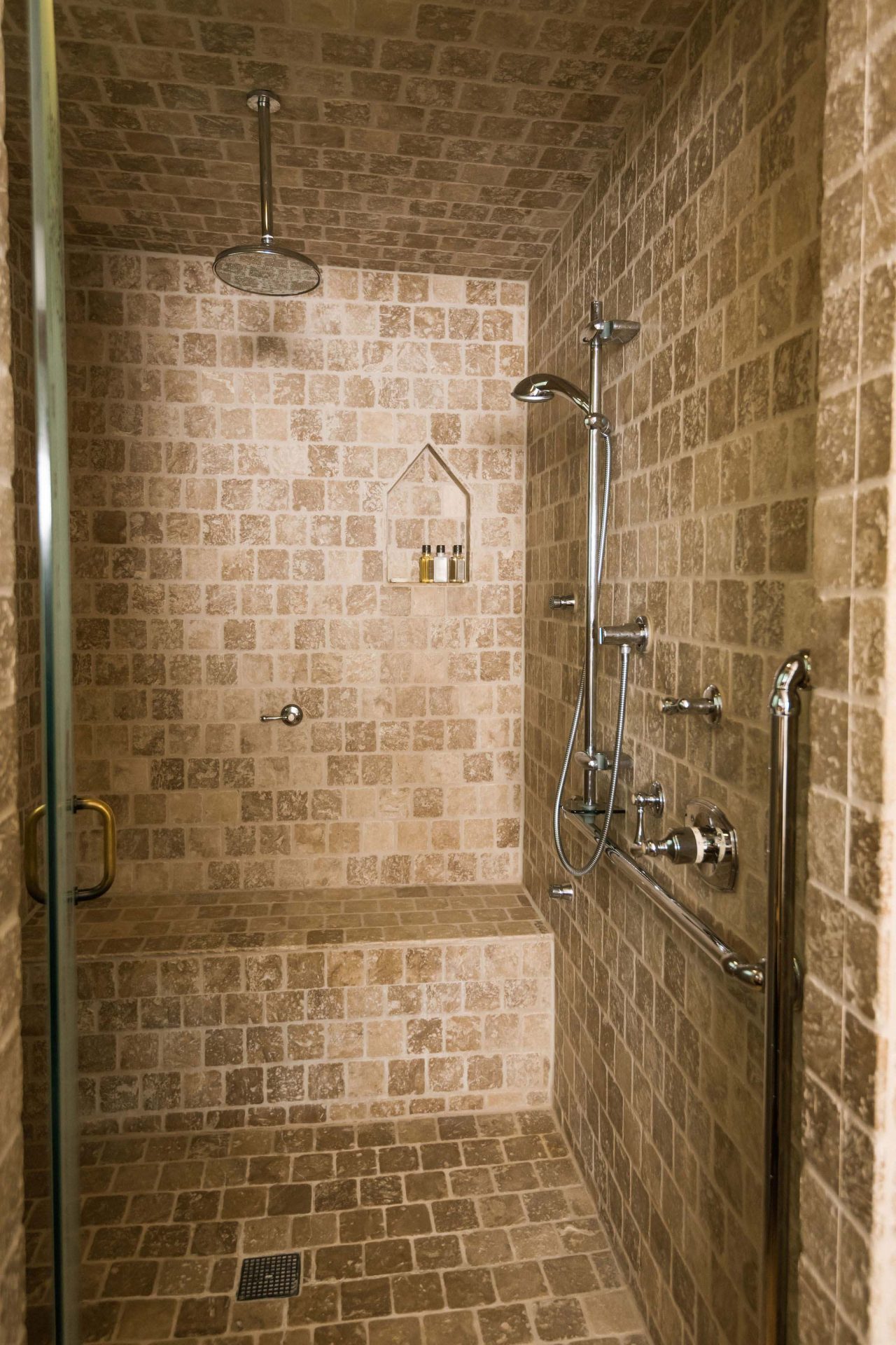 Shower with multiple body jets and steam bath, with beige-brown tiles.