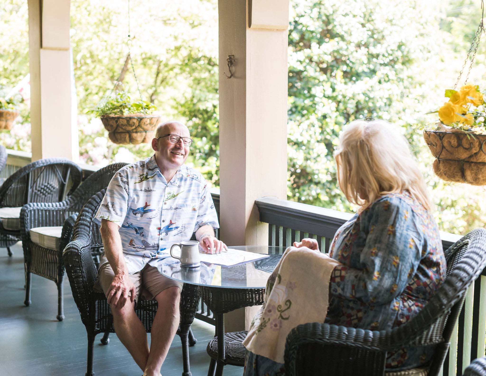 The Innkeepers enjoying coffee on the porch. Willy smiling at Shawnie who is embroidering.