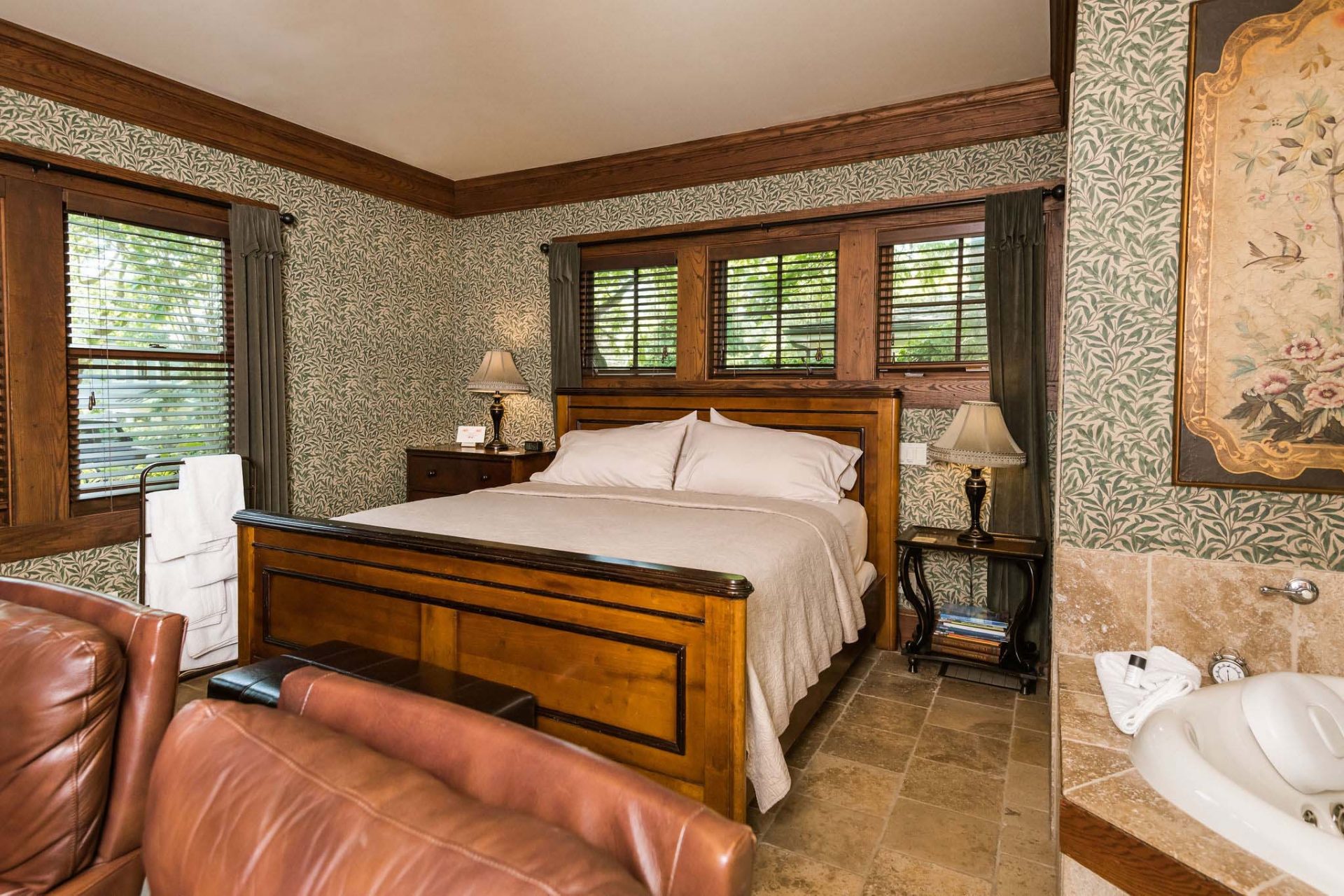 A pet-friendly room on the ground floor with beige tiles and a floral wallpaper. A king bed with two night stands and lamps, two leather club chairs, a multi-jet two-person Whirlpool.