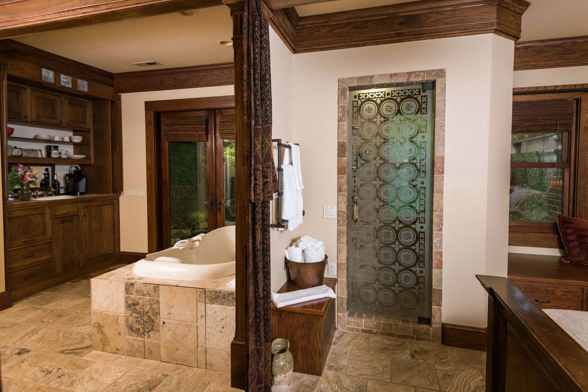 A small, dark wood kitchen area with a multi-jet two-person Whirlpool and the back doors opening onto a private rear garden, separated with a decorative curtain from the other room with king bedroom and a steam shower.