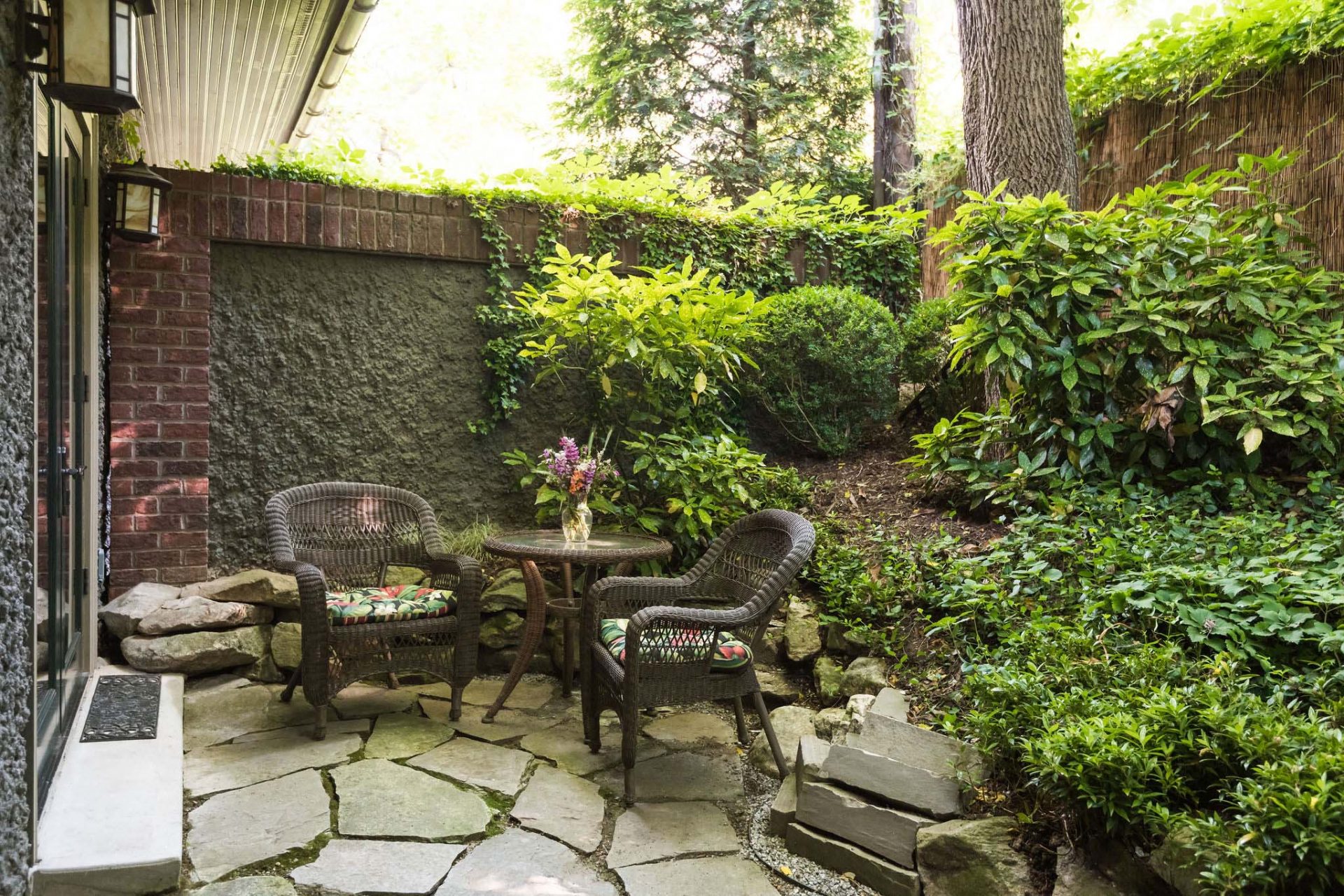 A private enclosed rear garden with two rattan chairs with cushions and a glass table with a flower bouquet.