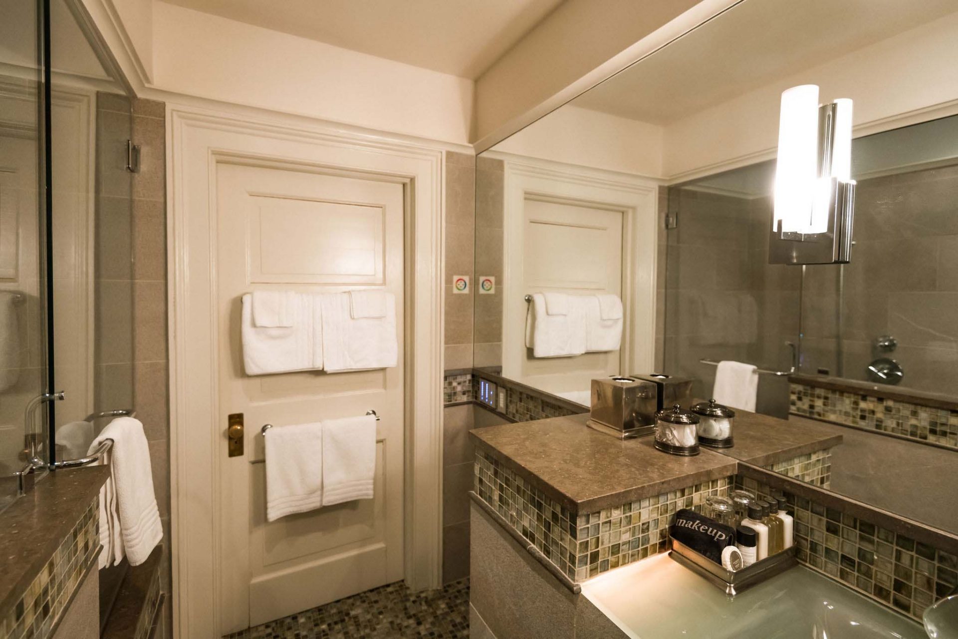 A luxurious bath with colorful fiber optic lighting and a blue-lit glass sink. White door with multiple towels and a long mirror above the sink.