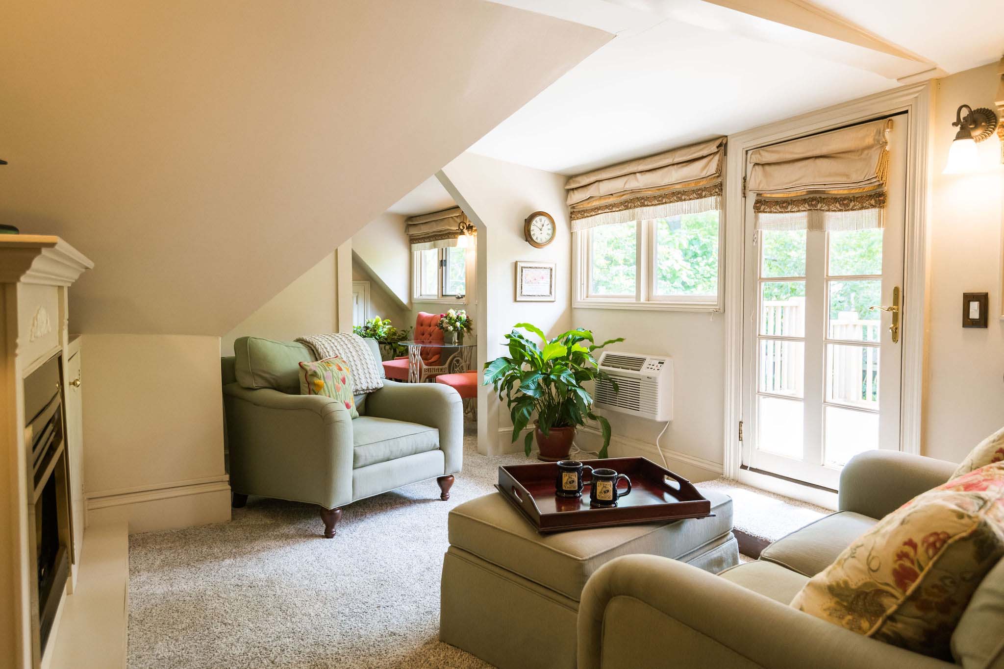 Sitting room in a 5-room suite of the Asheville Inn on Montford overlooking a private deck with a fireplace, a green couch, an armchair and a pouff.