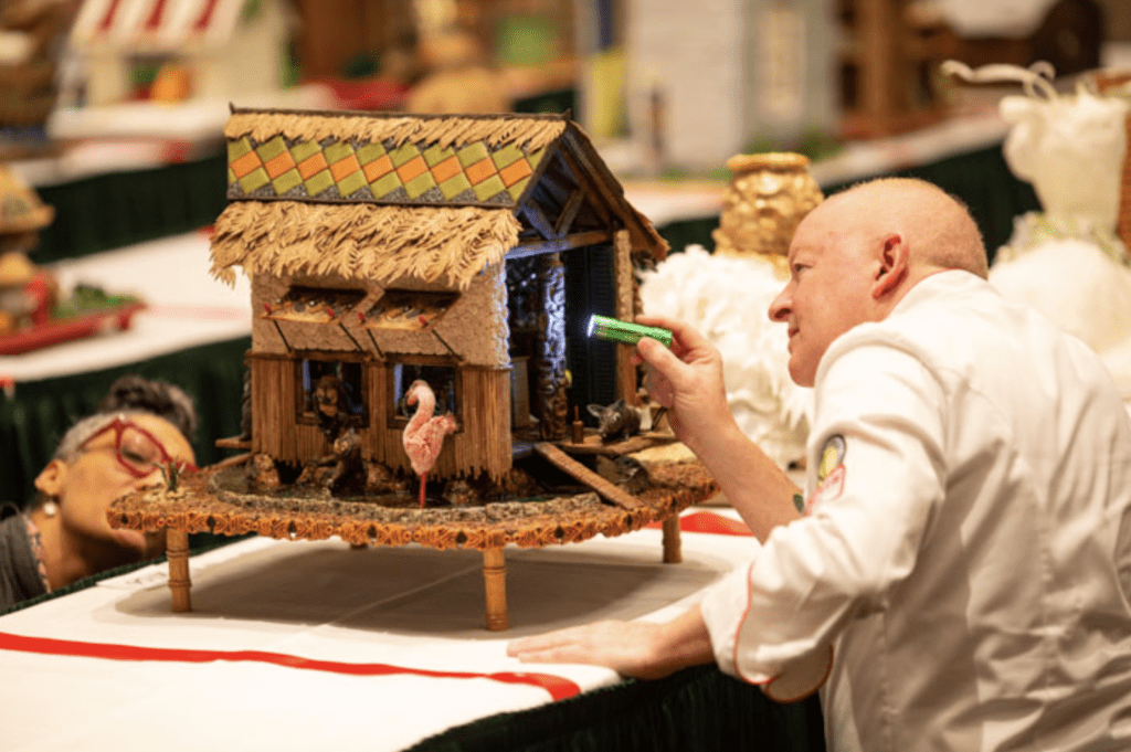 A photo of a man finishing his gingerbread house at the National Gingerbread House Competition.